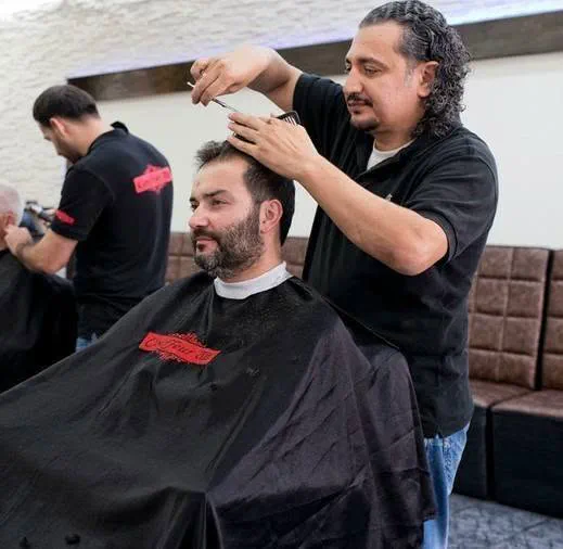 Ein Coiffeur schneidet einem Kunden mit Bart die Haare